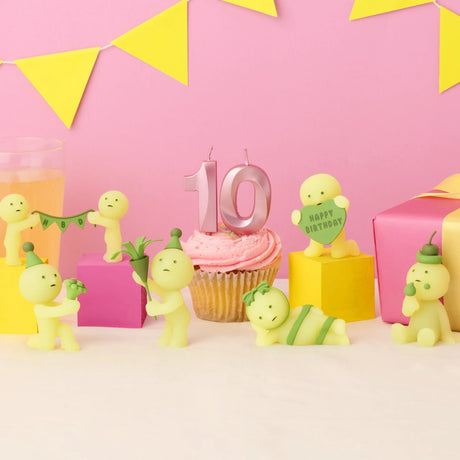 Smiski Birthday Series - Blind Box figurines by Smiski, featuring party props and glow-in-the-dark surprises, surround a cupcake with a "10" candle against a festive pink-and-yellow birthday-themed background with gifts and decorations.