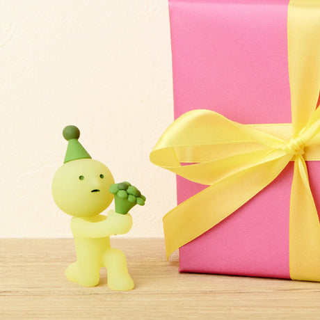 The Smiski Birthday Series - Blind Box by Smiski features a small yellow figurine kneeling with a bouquet beside a pink gift box with a yellow ribbon—an ideal find for Blind Box collectors.