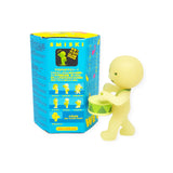 A small yellow glow-in-the-dark figurine from the Smiski brand's Cheer Series, holding a drum beside a bright blue blind box labeled with descriptions and images of these collectible figures.