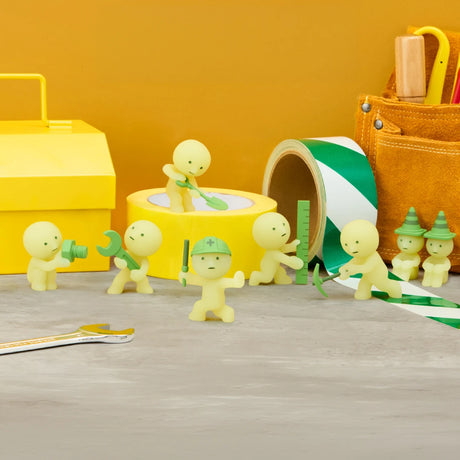 Smiski construction figure holding tools, light green, standing next to yellow storage box