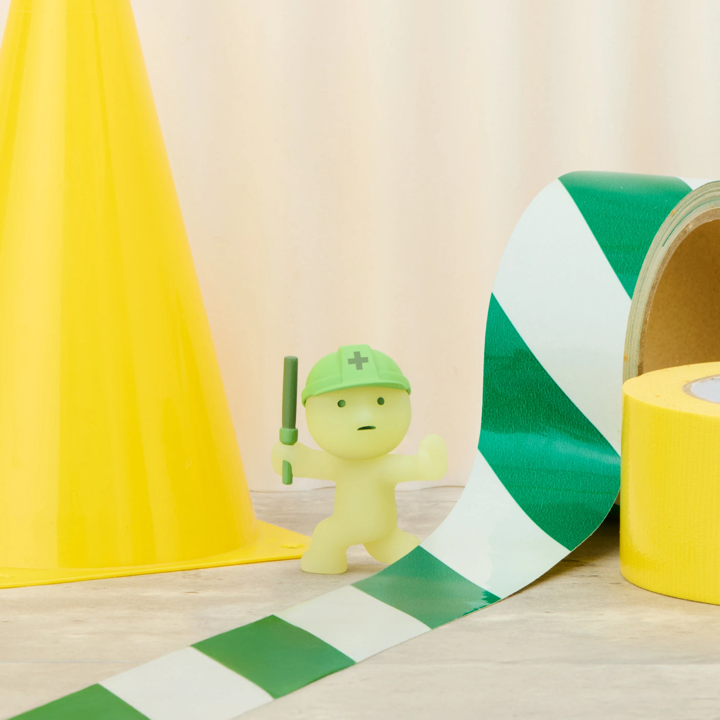 Smiski construction figure in green helmet, light green mini next to green-striped tape roll