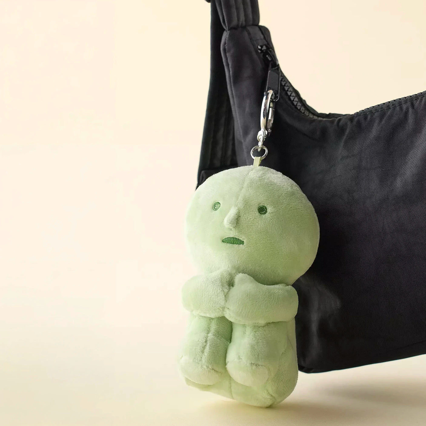Light green plush doll keychain with small limbs hanging from black fabric bag strap