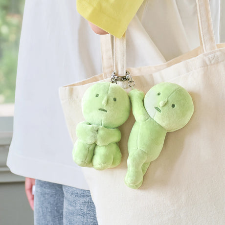 Two light green Smiski plush keychains attached to beige tote bag handles with silver keyrings