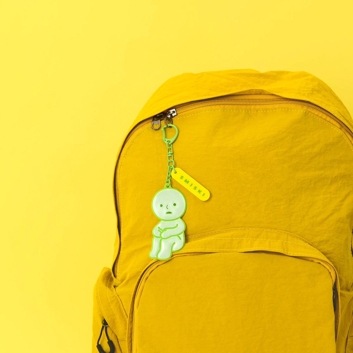 Reflective green Smiski charm on chain hanging from yellow backpack