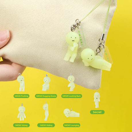 Miniature glow-in-the-dark Smiski figures in various poses attached to beige pouch against yellow background