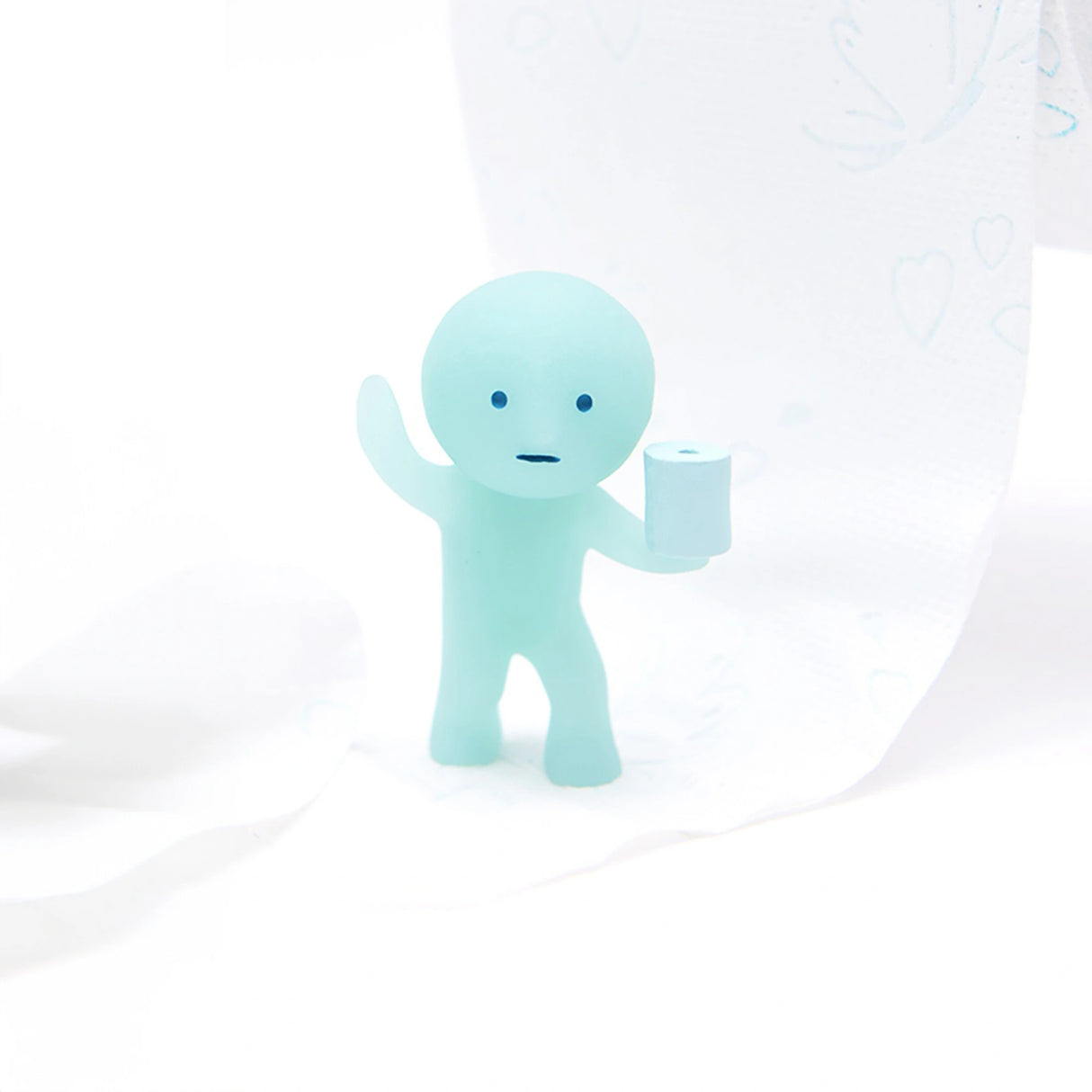 A figure from the Smiski Toilet Series - Blind Box by Smiski holds a toilet paper roll against a soft, white background. This small blue collectible brings charm to any space.