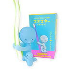 A Smiski Toothbrush Holder - Hugging Figure, notable for its collectible appeal, gently supports a toothbrush and emits a subtle glow in the dark. The original packaging stands prominently in the background, adding to its allure.