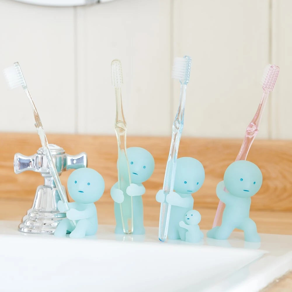 Four Smiski Toothbrush Holders - Holding Figures, each in a small blue design, clutch brushes of various colors on a bathroom sink. They not only keep your bathroom organized and fun but also add a whimsical touch with their glow-in-the-dark feature next to the faucet.