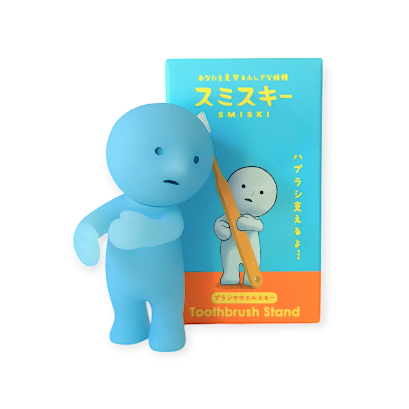 A delightful blue cartoon character, known as the Smiski Toothbrush Holder - Holding Figure, features next to its glow-in-the-dark counterpart on a vibrant box adorned with Japanese text in shades of blue and orange, making it an ideal choice for organizing your bathroom.