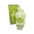 A Smiski Touch Light, featuring a glowing green figurine with a cat-like figure atop its head and functioning as a touch-activated nightlight, is placed next to its matching box labeled "Smiski Touch Light.