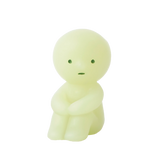 A compact, round-headed figurine in a gentle shade of green sits with its arms resting on its knees and showcases minimal facial features. This Smiski ZipperBite - Hugging Knees from the Smiski brand is a glow-in-the-dark zipper accessory that brings a whimsical charm to your belongings.