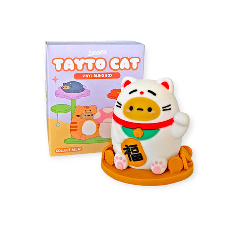 A white cat figurine with a red and green scarf stands proudly in front of a "Smoko Tayto Cat Blind Box." The box features playful cat illustrations from Smoko, inviting you to "Collect all 6!.