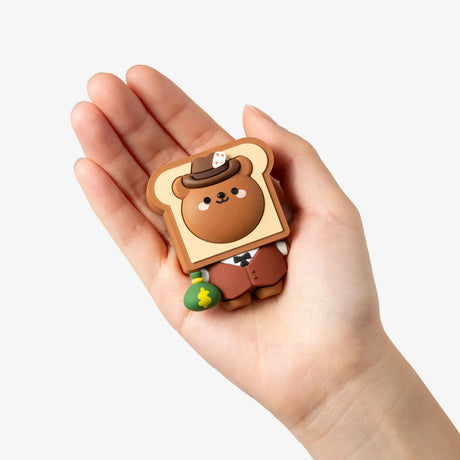 Small brown bear figurine dressed in a suit and hat holding a green money bag, held in a hand against a white background