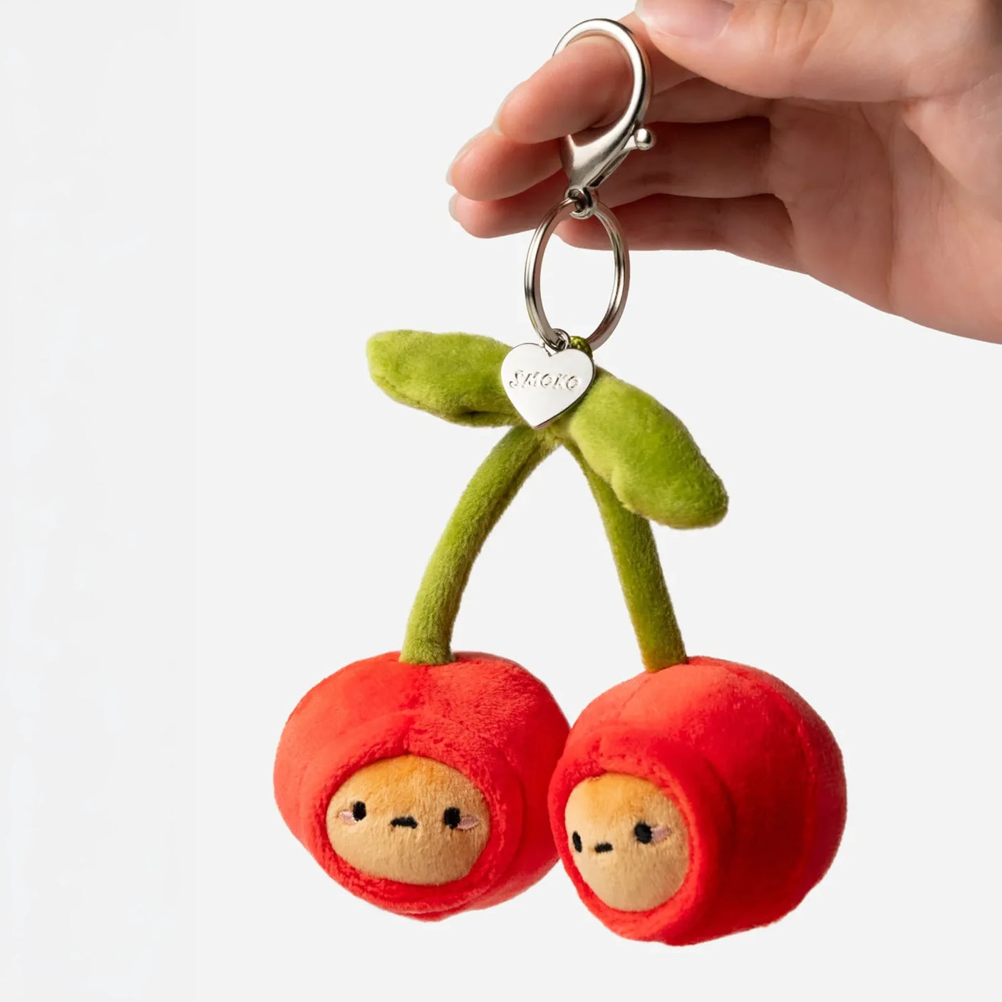 Plush cherry bag charm with metal keyring held by hand; green leaves and two red faces