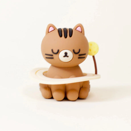 A small brown Smoko Astrocats Blind Box cartoon cat figurine with closed eyes sits in a cream ring with a yellow ball, set against a white background—an adorable collectible from Smoko.