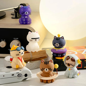 Six Smoko Astrocats Blind Box vinyl figures, each in a different costume, are displayed on a white table next to a lamp, radio, and camera.