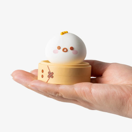 Hand holding a white Smoko Dim Sum Friends vinyl figure designed like a cute steamed bun inside a tan steamer basket