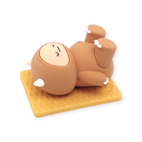 Brown Smoko Hank Yeti figure lying on back with eyes closed on textured tan mat against white background