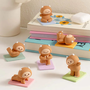 Six Smoko Hank Yeti Doing Yoga blind box figures posed on colorful mats with stacked books in soft background lighting