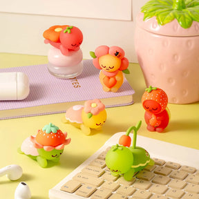 Six sleepy Smoko Kawawa Turtle figures wearing fruit and flower costumes on a desk with keyboard and plant nearby