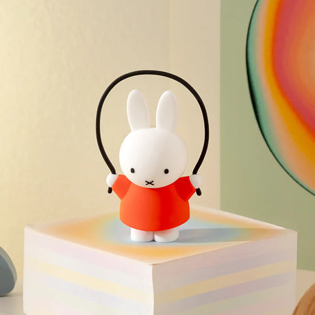 White bunny figurine in an orange dress holding a black jump rope standing on a pastel-colored block