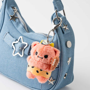 Orange plush oni keychain with smiling face and star accents, on denim bag strap