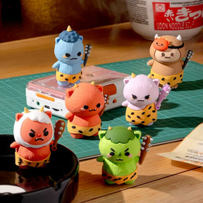 Six vibrant, cartoon-style vinyl figures from Smoko’s Roni And Oni Bunch Blind Box stand on a green cutting mat by a cassette player and cup noodles—fun collectible toys for any playful display.