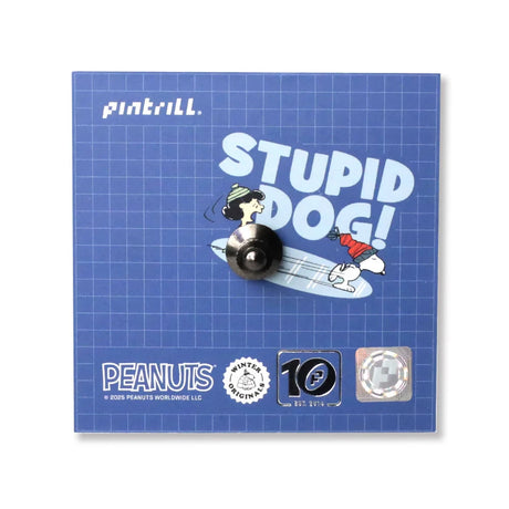 A blue backing card displays the Snoopy Puffer Jacket Pin, featuring Snoopy surfing with Woodstock on his tail and Lucy chasing him. "STUPID DOG!" appears above, with Snoopy branding at the bottom.