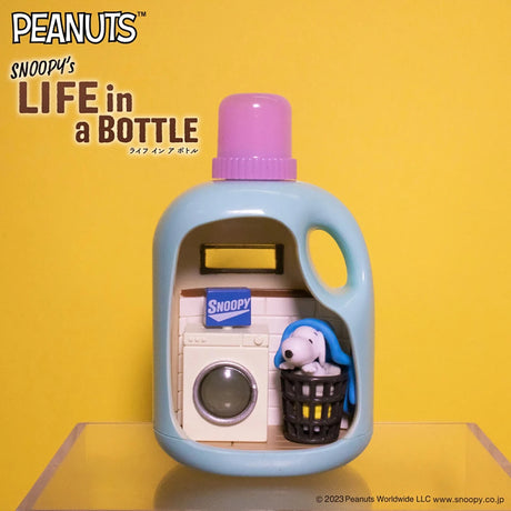 Blue bottle diorama with Snoopy sleeping on laundry basket next to washing machine against yellow background