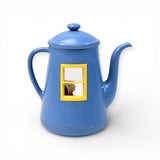Blue ceramic teapot figurine with yellow window frame showing Snoopy peeking through inside