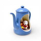 Blue teapot figurine with Snoopy holding a red cup and Woodstock inside a cozy cutout scene