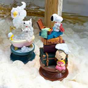 Two spiral dioramas showing Snoopy and Woodstock in bathtub clouds and Charlie Brown with stacked suitcases scenes