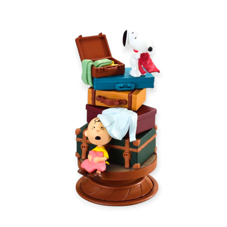 Stacked vintage suitcases with Snoopy holding a red cloth and Charlie Brown resting with a blanket on rotating base