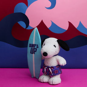 Snoopy plush wearing purple floral board shorts standing next to blue surfboard with Surf's Up text, colorful wave backdrop