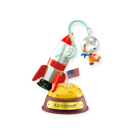 Snoopy in orange astronaut suit floating by red and silver rocket with moon base and US flag on Astronaut plaque