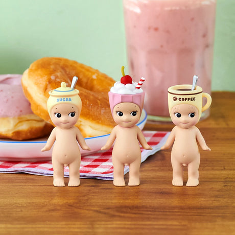 Three Sonny Angel Snack Series - Blind Box mini-figures by Sonny Angel stand adorned with snack-themed hats—a sugar jar, dessert cup with cherry, and coffee mug—surrounded by donuts and a pink drink for extra charm.
