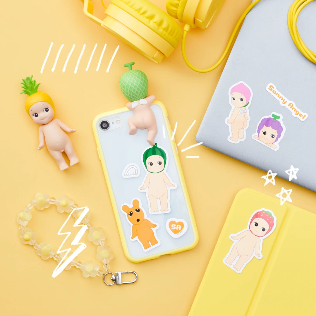 A phone case decorated with charming stickers from the Sonny Angel Blind Box - Sticker Pack Series 2 by Sonny Angel is surrounded by figurines, yellow headphones, a bracelet, and a yellow notebook on a vibrant yellow background.