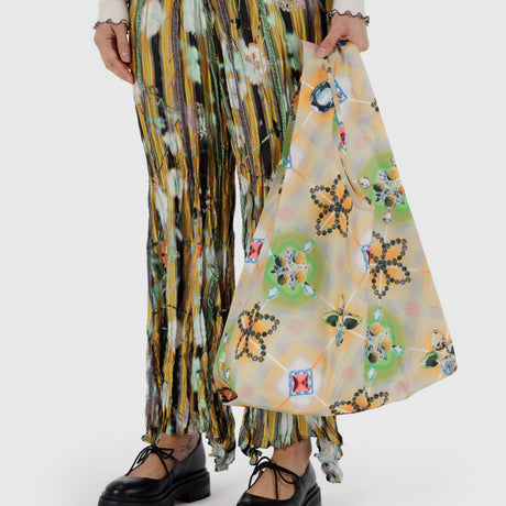 A person carries the Standard Baggu x Julia Heuer - Raisa tote, made of colorful recycled ripstop nylon, complementing their patterned skirt and black shoes.