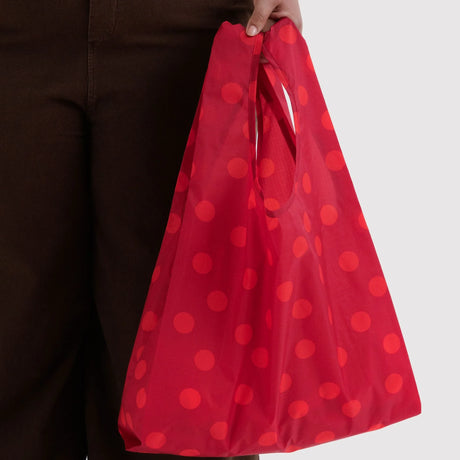 Baggu standard reusable tote bag in red polka dots, carried by hand