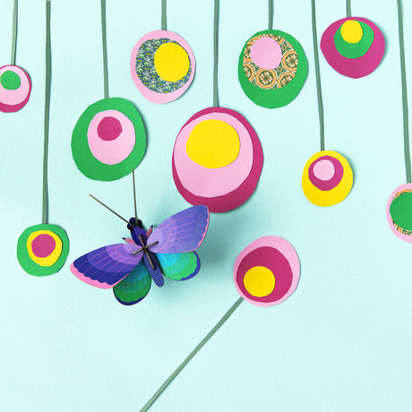 The Wall Art Puzzle - Blue Copper Butterfly by Studio Roof features a vibrant butterfly set among pink, yellow, and green hanging circles on a light blue background, creating a lively 3D sculpture effect.