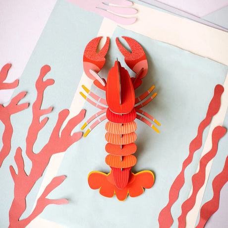 Top-down view of a vibrant 3D lobster wall art puzzle assembled on pastel paper backdrop with coral-shaped cutouts