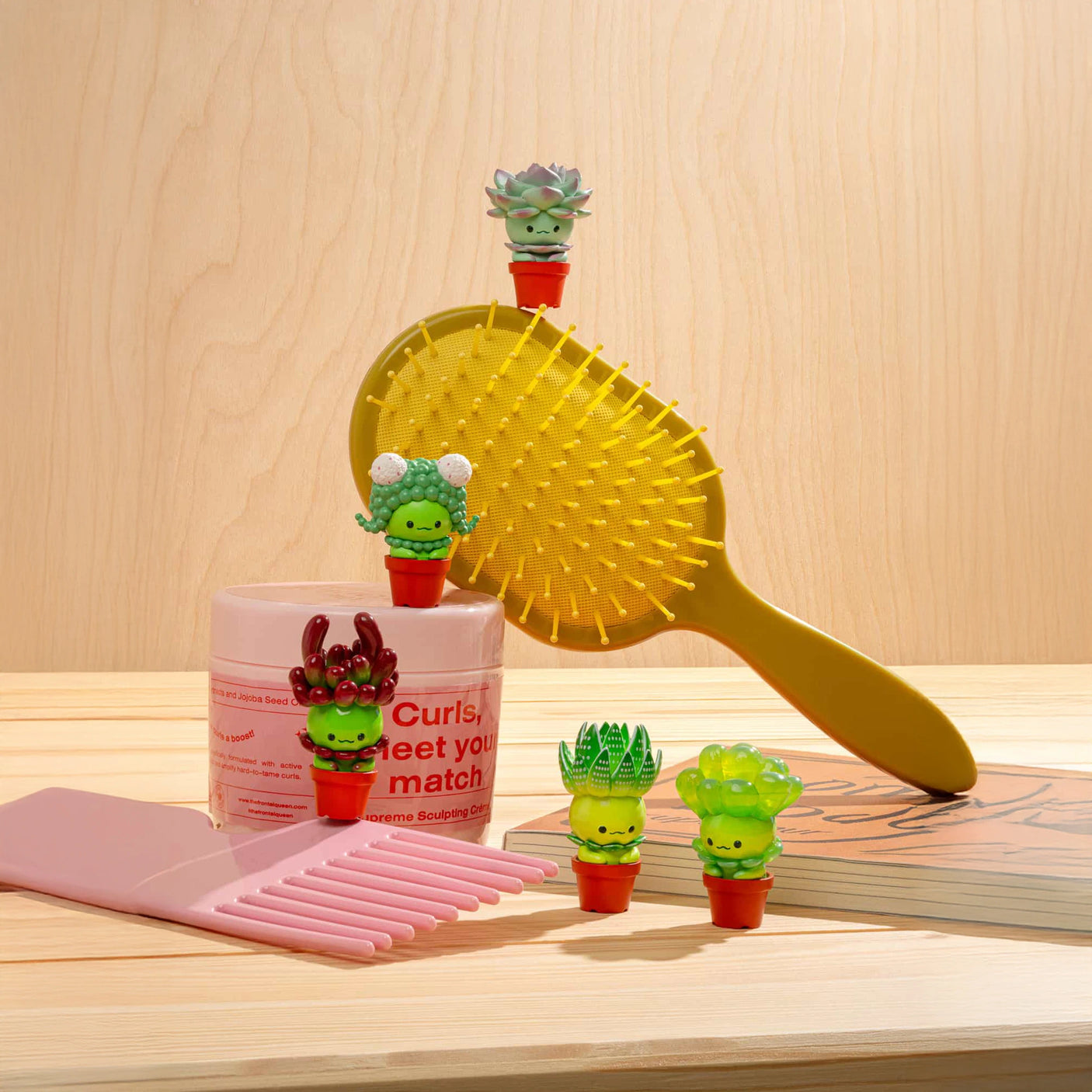 A yellow hairbrush and a pink comb are placed on a wooden surface with small decorations from the "Succulent Friends Blind Box" by Kitan Club, adding a touch of playful mystery to the scene.