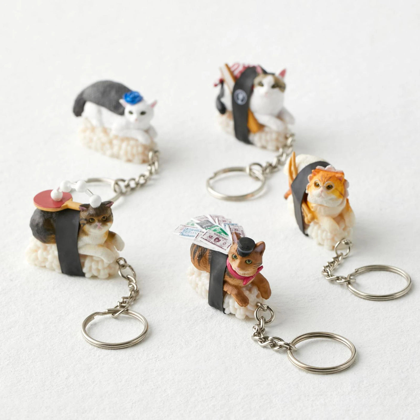 Explore the delightful Mofusand Sushi Cat Keychain Blind Box - Vol.2 set, featuring five charming keychains. Each adorable keychain resembles a sushi roll with unique toppings and accessories, elegantly arranged on a light surface.