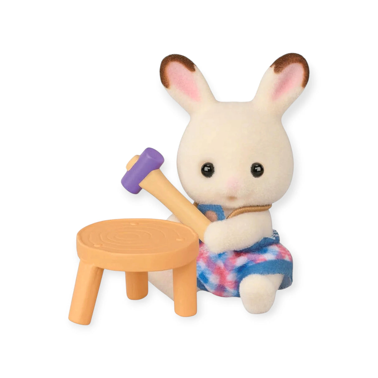 The Sylvanian Families Blind Bag - Baby Builder features a small rabbit in a blue and pink dress with a mallet, sitting by an orange table—ideal for Sylvanian Families collectors and fans of cute baby figures.