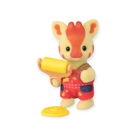 A Sylvanian Families Blind Bag - Baby Builder figure by Sylvanian Families features a small toy giraffe in red overalls holding a yellow paint roller beside a puddle of yellow paint on a white background.