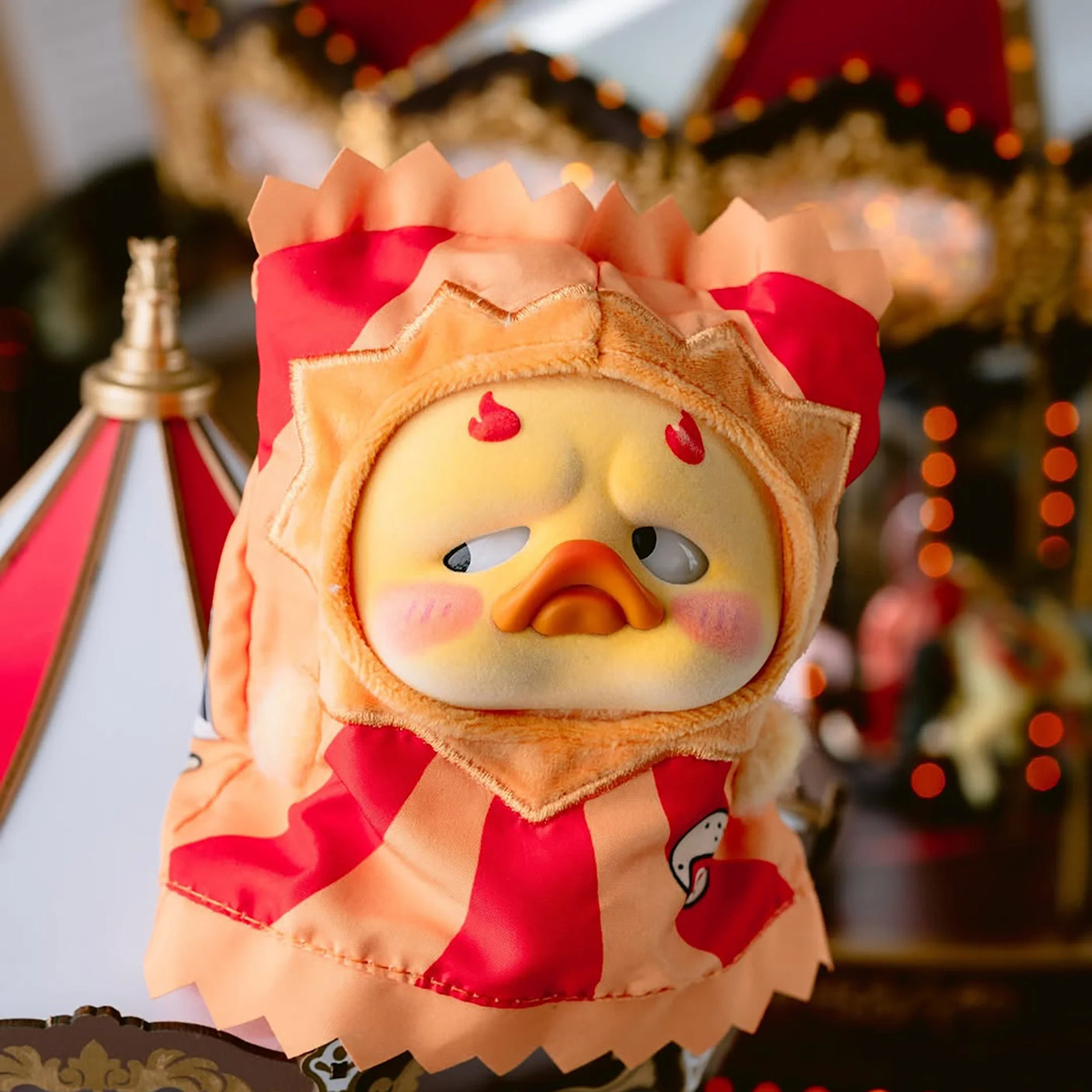 Circus-themed vinyl plush duck with red-and-tan hood, smiling face, charm.