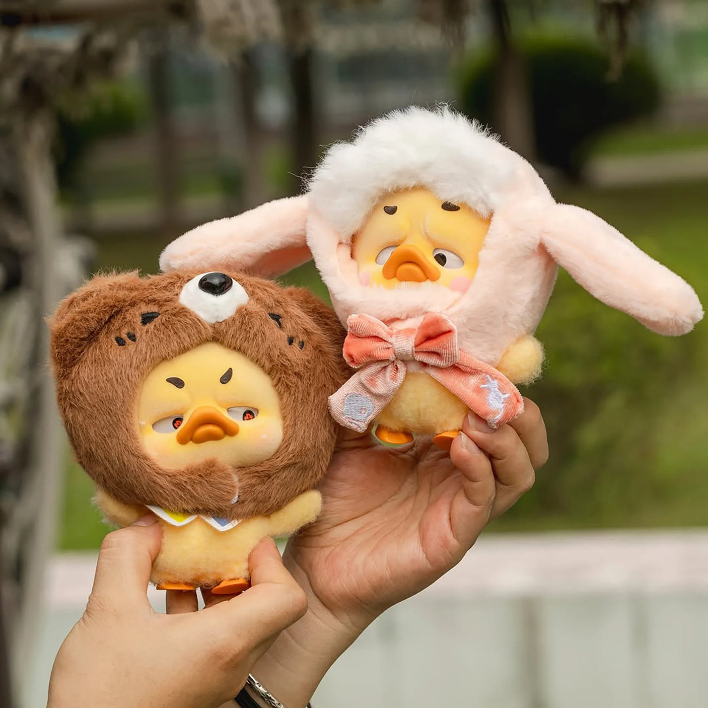 Two plush duck characters: brown bear hood and white bunny hood held in hands