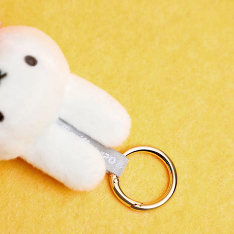 Close-up of white plush bunny keychain attached to gold metal ring on bright yellow background
