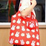 Red tote bag with white bunny and flower pattern held by a person