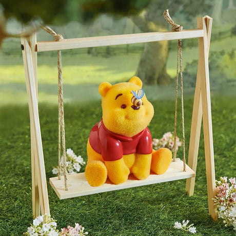 Yellow bear figurine in red shirt sitting on wooden swing with a small blue butterfly on its nose outdoors